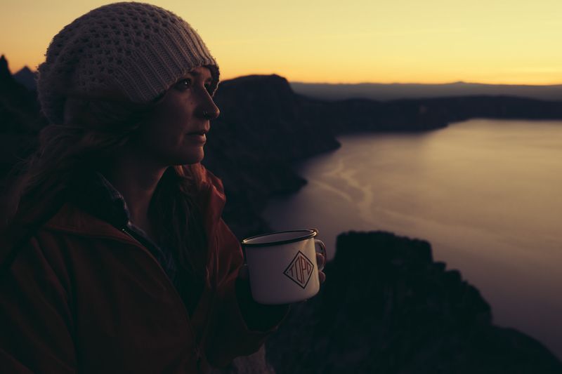 woman drinking coffee at sunrise over crater lake